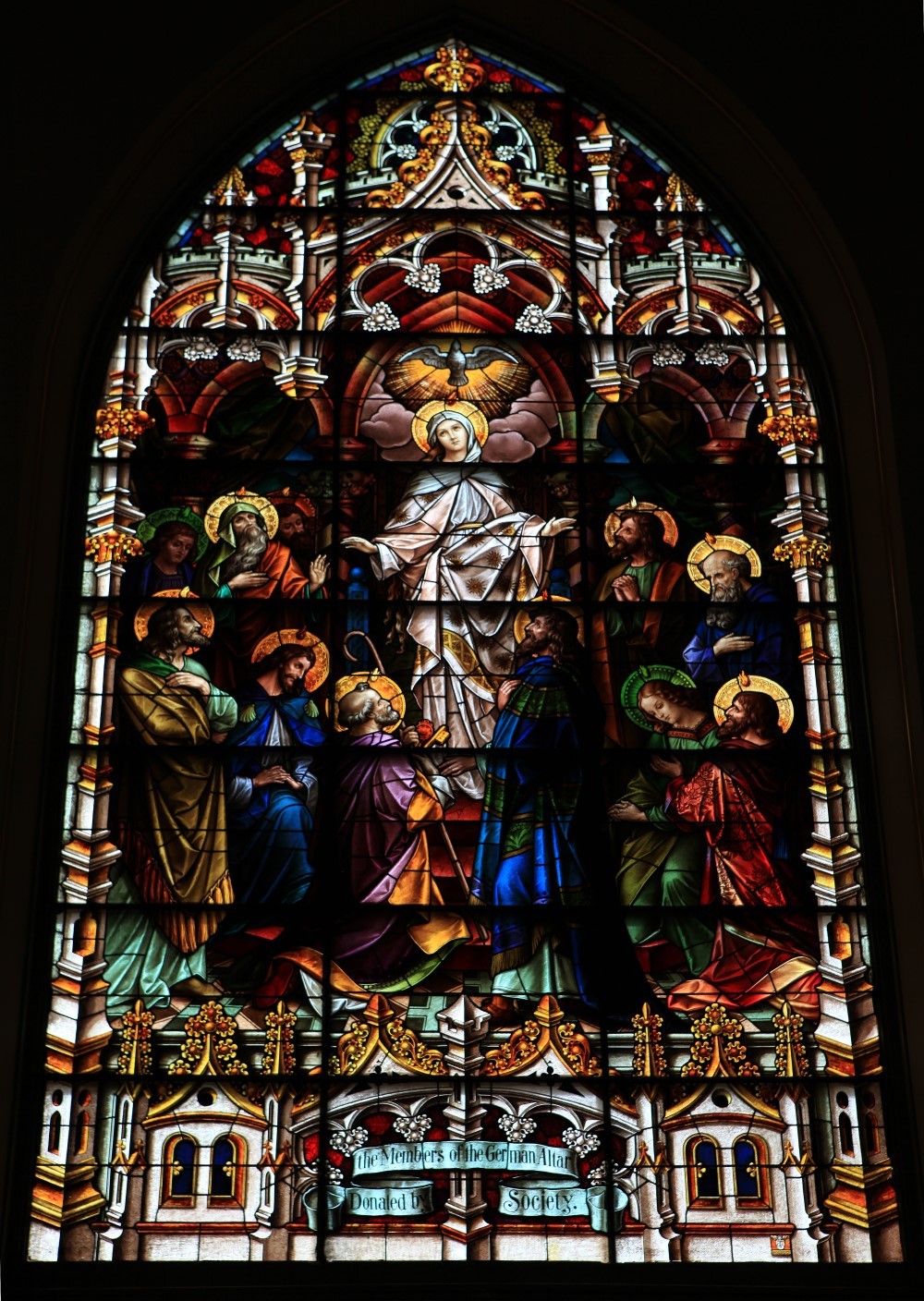 Grand historic stained glass window showing detailed figural scenes and ornate architectural framing